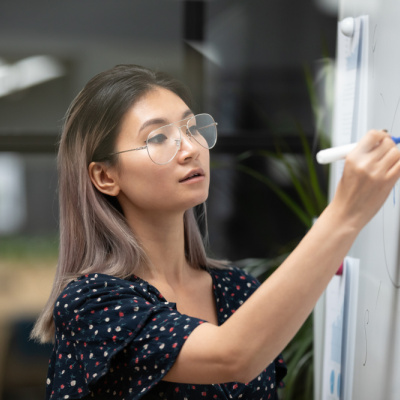 A female teacher concentrates while drawing graphs on a white board, giving a presentation on pedagogy to her colleagues.
