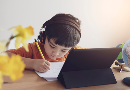 Schoolboy wearing headphones and listening information from his digital tablet.,