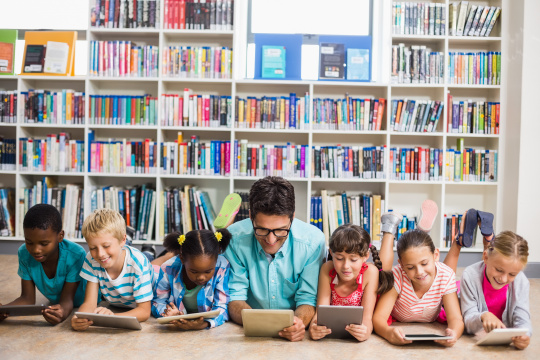 Teacher and students lying on the floor using digital tablet in a school library.