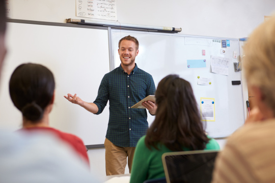 Male teacher listening to students at adult education class.