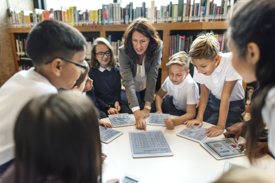 A school teacher explains a concept to a group of students using electronic tablets.