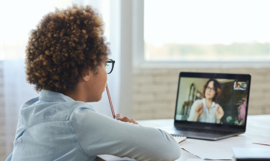 A schoolgirl listens to her teacher during online video lesson while studying from home.