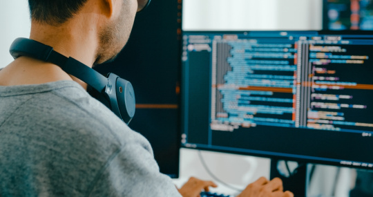 Developer with headphones slung around neck writing code for a learning application. 