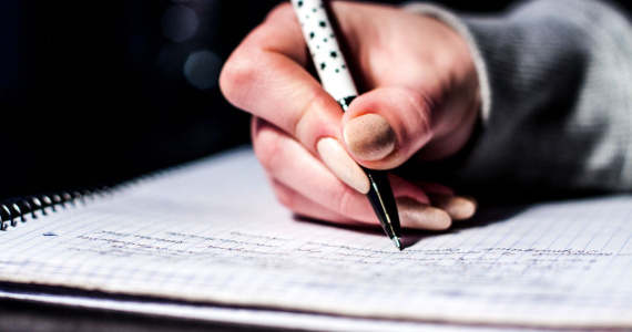 Hand holding a pen writing in a spiral notebook