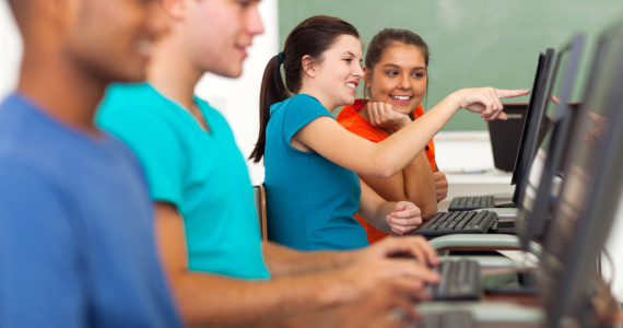Teenage high school girl helping a classmate with computer in class