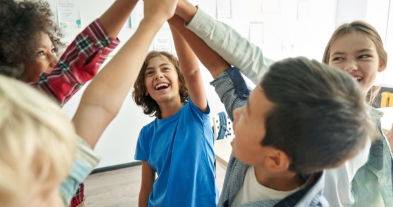 Happy junior high school students giving each other high fives in the classroom. 