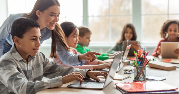 Teacher teaching diverse school kids using laptop in a classroom. 