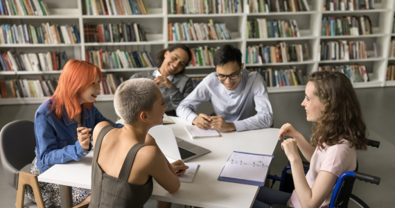A happy group of students study in a school library, talking and laughing.