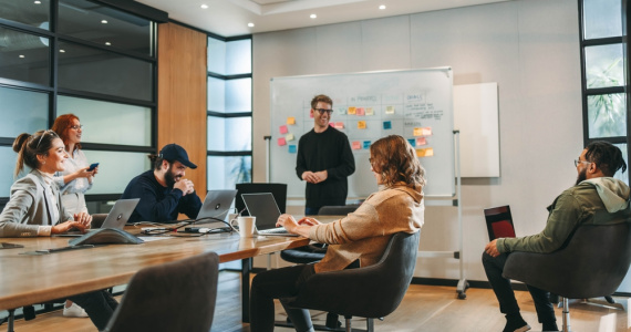 Professionals in a diverse group collaborate in a boardroom, engaging in a lively brainstorming session. They discuss ideas, showcasing teamwork and creativity. 