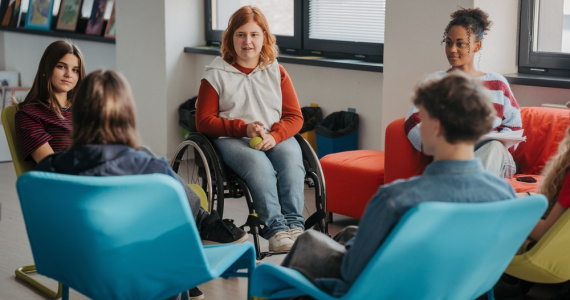 Young female student using wheelchair collaborates with classmates in the school library.