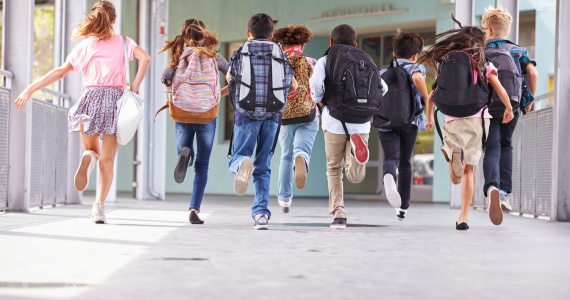 A diverse group of younger students wearing backpacks running to recess.