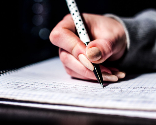 Hand holding a pen writing in a spiral notebook