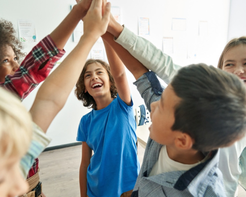 Happy junior high school students giving each other high fives in the classroom. 