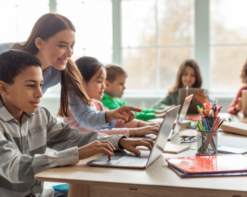 Teacher teaching diverse school kids using laptop in a classroom. 