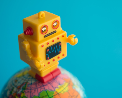 Cute yellow robot stands on a globe of the earth with blue background. 